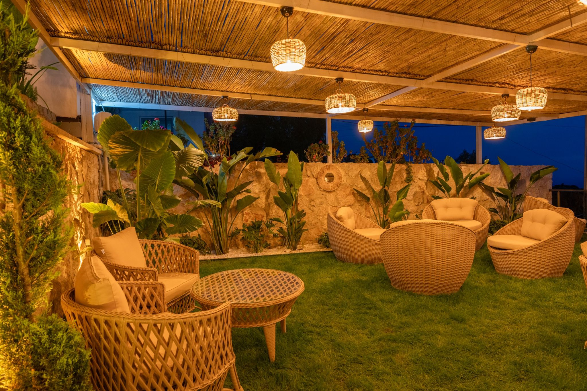 Modern terracotta type wooden wicker chairs with white cushions and table, sitting in lush green grass with palm trees, pl...