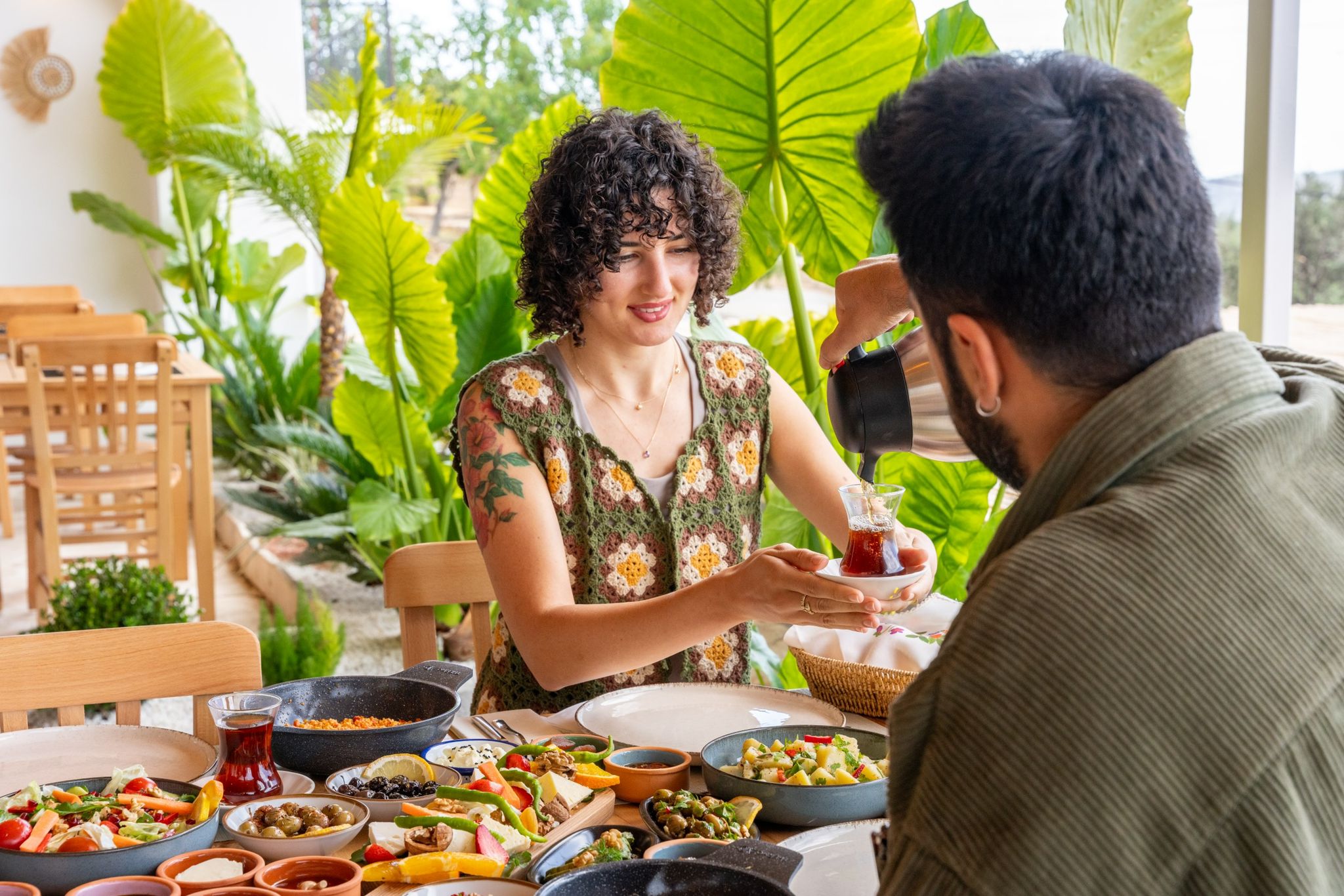 A woman is serving a man with an ear of corn in his shirt. She is a young woman with curly black hair. She is wearing a mi...